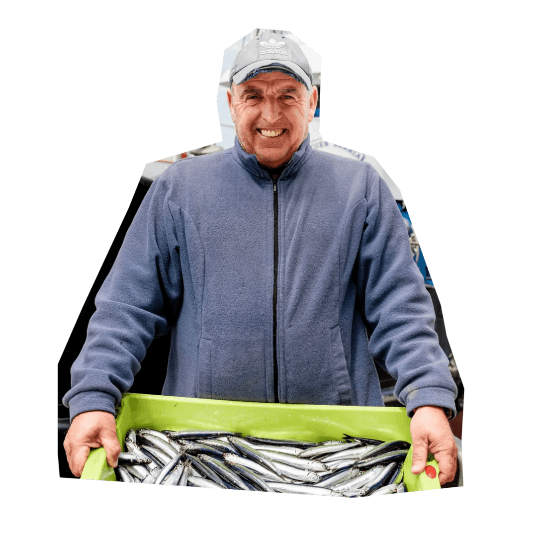 Smiling man in a cap holding a green crate filled with freshly caught fish.